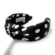 Load image into Gallery viewer, Black headband with white polka dots, featuring a twisted knot design. A label inside reads "Twine and Love." The style is stylish and playful.