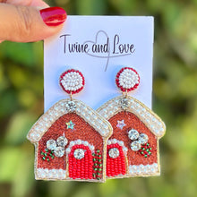 Load image into Gallery viewer, Red house-shaped earrings on a card held by a hand with a blurred green background