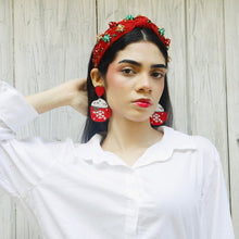 Load image into Gallery viewer, Woman wearing a white shirt with red and green headband and earrings against a wooden background