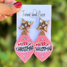 Load image into Gallery viewer, Pink beaded earrings shaped like Christmas ornaments with "Merry Christmas" text. Each has a star-shaped top, conveying festive cheer.