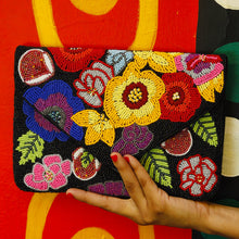 Load image into Gallery viewer, Hand holding a colorful beaded clutch against a red background with yellow swirls.