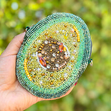 Load image into Gallery viewer, Hand holding a beaded avocado pouch against a blurred green background