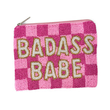 Load image into Gallery viewer, A pink beaded zip pouch with a pink and magenta checkered pattern, featuring the words 'BADASS BABE' in cream-colored beads with gold outlines. A silver metal zipper pull is visible at the top left.