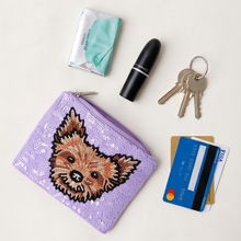 Load image into Gallery viewer, A lavender purple sequined coin purse with a detailed beaded dog face on the front, styled in a flat-lay arrangement with a lipstick, keys, cards, and a tissue on a light cream background.