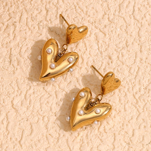 18k Gold plated heart-shaped earrings with pearl accents on a beige textured background