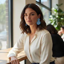 Load image into Gallery viewer, Woman sitting at a table in a modern indoor setting with large windows.