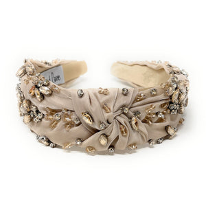 Elegant beige headband adorned with sparkling crystals and gemstones. The luxurious fabric is delicately ruched, creating a sophisticated and glamorous look.