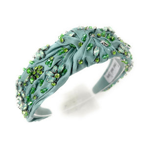 Elegant green headband adorned with sparkling crystals and gemstones. The luxurious fabric is delicately ruched, creating a sophisticated and glamorous look.