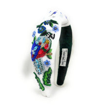 Load image into Gallery viewer, White hand-beaded knotted headband featuring a colorful jeweled bird, blue flowers, green leaves, and sparkling crystal embellishments. Handmade statement hair accessory by Twine and Love.