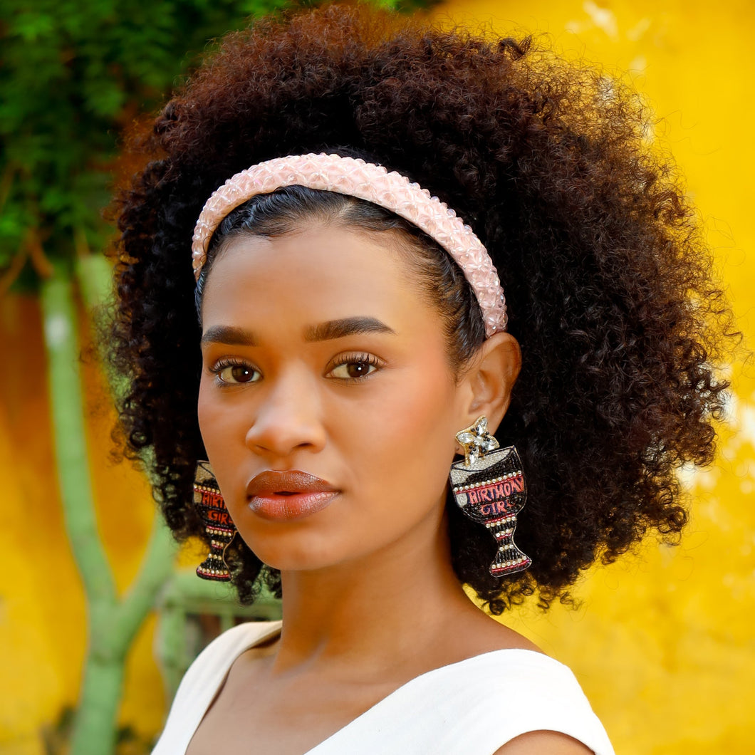 Woman with curly hair wearing a pink headband and earrings against a yellow background