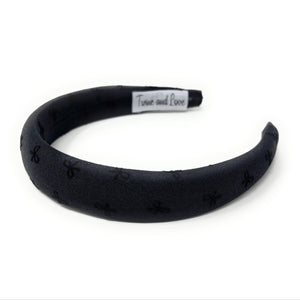 Elegant black fabric headband with subtle bow pattern. Minimalist and chic.