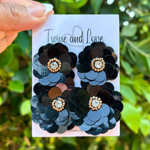 Load image into Gallery viewer, Black sequin earrings on a card held in front of green foliage