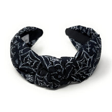 Load image into Gallery viewer, A black fabric headband with a knotted design is patterned with white spiderwebs and spiders. The mood is edgy and Halloween-themed.