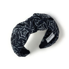 Load image into Gallery viewer, A black fabric headband with a knotted design is patterned with white spiderwebs and spiders. The mood is edgy and Halloween-themed.