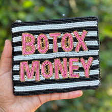 Load image into Gallery viewer, A hand holds a small zippered pouch with black and white stripes and the words 'BOTOX MONEY' in pink and gold lettering, set against a blurred green outdoor background.