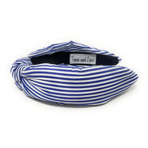 Blue and white striped headband with a knotted detail in the center, set against a plain white background, conveying a trendy, nautical style.