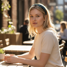 Load image into Gallery viewer, Woman sitting at an outdoor cafe table in a city setting with a blue headband