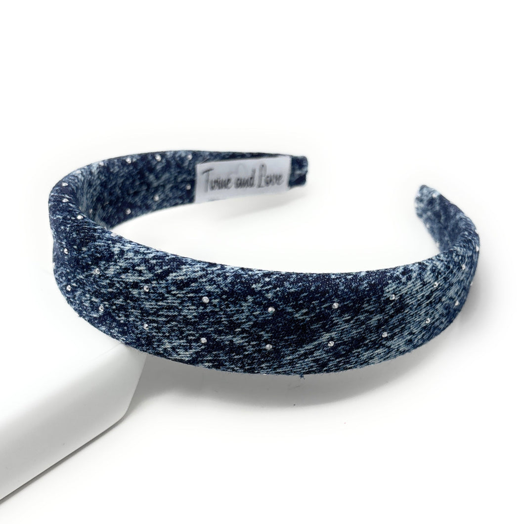 Dark blue denim headband with a textured pattern and rhinestones. The headband has a tag and lies on a white background.