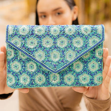 Load image into Gallery viewer, Person holding a blue and green patterned clutch in front of their face with a blurred natural background
