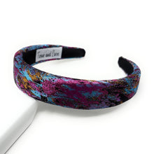 Load image into Gallery viewer, Elegant headband with a vibrant pattern of pink, blue, and gold accents on a textured fabric. It rests on a white surface, exuding a bold, stylish tone.