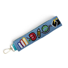 Load image into Gallery viewer, A blue beaded keychain strap featuring colorful symbols representing school subjects (pencils, apple, book, paintbrush, globe, and flag) with a gold metal lobster clasp on a white background.