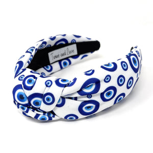 White and blue headband with a knot design featuring an evil eye pattern. The design is vibrant and playful, giving a trendy and stylish feel.