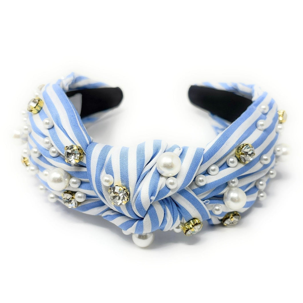 A stylish headband with blue and white stripes, adorned with pearls and sparkling gems. It has a knotted design, offering a chic and elegant look.
