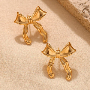 18k Gold plated bow-shaped earrings on a beige fabric background