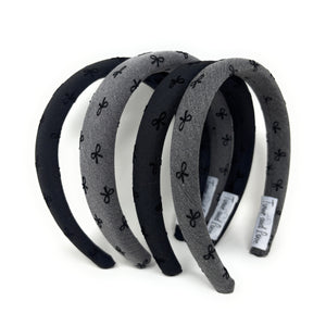 Four fabric headbands with bow patterns, alternating in black and gray, are stacked in a semi-circle on a white background.