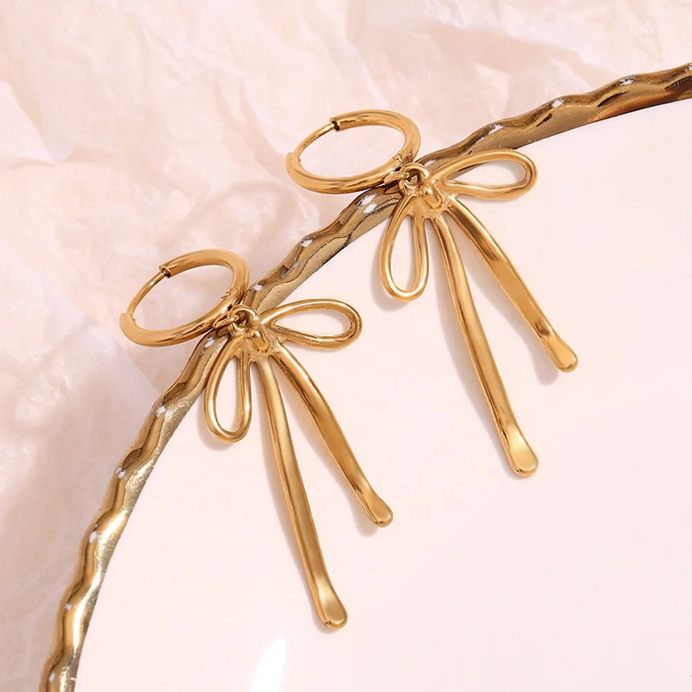 Gold earrings with abstract bow shapes and dangling elements. The design is modern and elegant, suggesting a stylish and artistic flair.