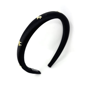 Elegant black satin headband adorned with small gold bow embellishments, displayed against a plain white background, conveying a stylish and chic tone.