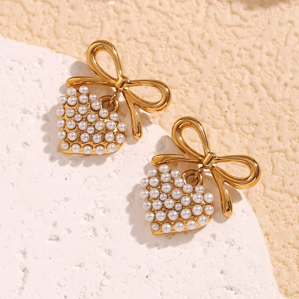 18k Gold plated earrings with bow and pearl details on a textured beige surface