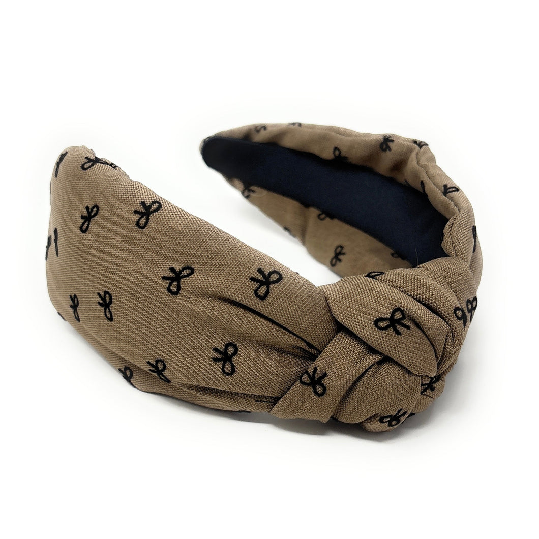 Brown headband with a knotted design, featuring small black bow patterns. The inside tag reads 