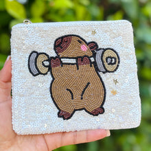 Load image into Gallery viewer, White sequined pouch with a cute capybara lifting weights design.