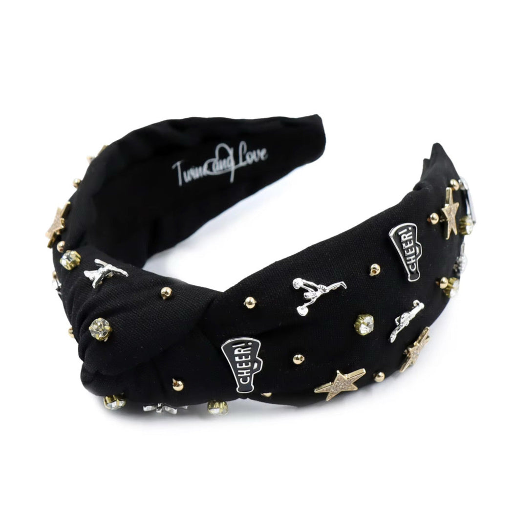 Black headband adorned with gold and silver embellishments, including stars, cheerleaders, and rhinestones, exuding a playful and glamorous vibe.