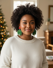Load image into Gallery viewer, Woman wearing a white sweater and green earrings with a Christmas tree in the background
