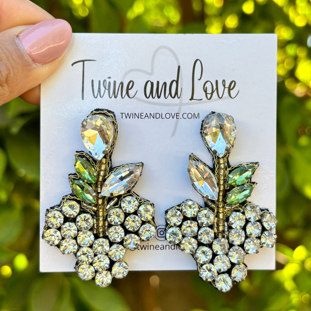 leaf-shaped earrings with crystal clusters. The background is green and leafy, enhancing a fresh, elegant vibe.