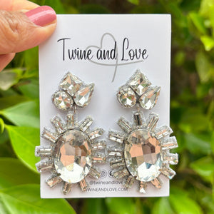 Elegant drop earrings featuring large, oval gemstones surrounded by smaller, radiant crystals on a white background, exuding a glamorous tone.