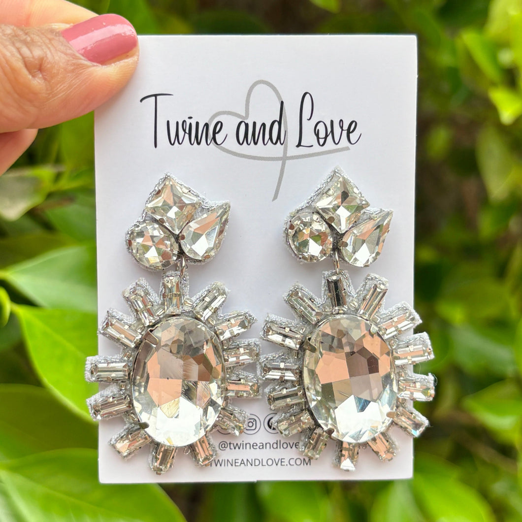 Elegant drop earrings featuring large, oval gemstones surrounded by smaller, radiant crystals on a white background, exuding a glamorous tone.