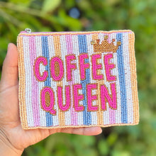 Load image into Gallery viewer, A hand holds a small zippered pouch outdoors against a blurred green foliage background. The pouch has vertical pastel stripes in pink, blue, yellow, and white, with the words 'COFFEE QUEEN' in large pink letters and a small gold crown above it.