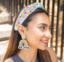 Load image into Gallery viewer, A joyful woman smiling while wearing colorful accessories, including a floral headband and rainbow earrings.