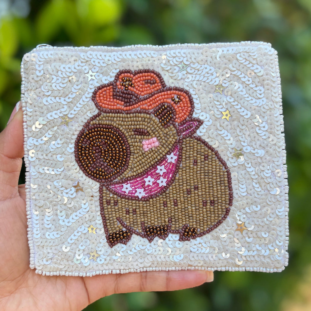 Sequined pouch featuring a cute capybara wearing an orange cowboy hat and pink bandana. Background covered in shiny white sequins, playful tone.