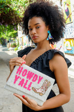 Load image into Gallery viewer, Woman holding a white hand-beaded clutch featuring bright pink “Howdy Y’all” lettering and a decorative cowboy boot design.