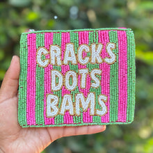 Load image into Gallery viewer, A hand holds a small rectangular beaded pouch with pink and green vertical stripes and white text reading 'CRACKS DOTS BAMS' against a blurred green outdoor background.