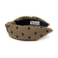 Load image into Gallery viewer, Brown headband with a knotted design, featuring small black bow patterns. The inside tag reads &quot;Time and Love.&quot; The tone is stylish and elegant.