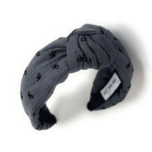 Load image into Gallery viewer, Smokey gray headband with a knotted design, featuring small black bow patterns. The inside tag reads &quot;Time and Love.&quot; The tone is stylish and elegant.