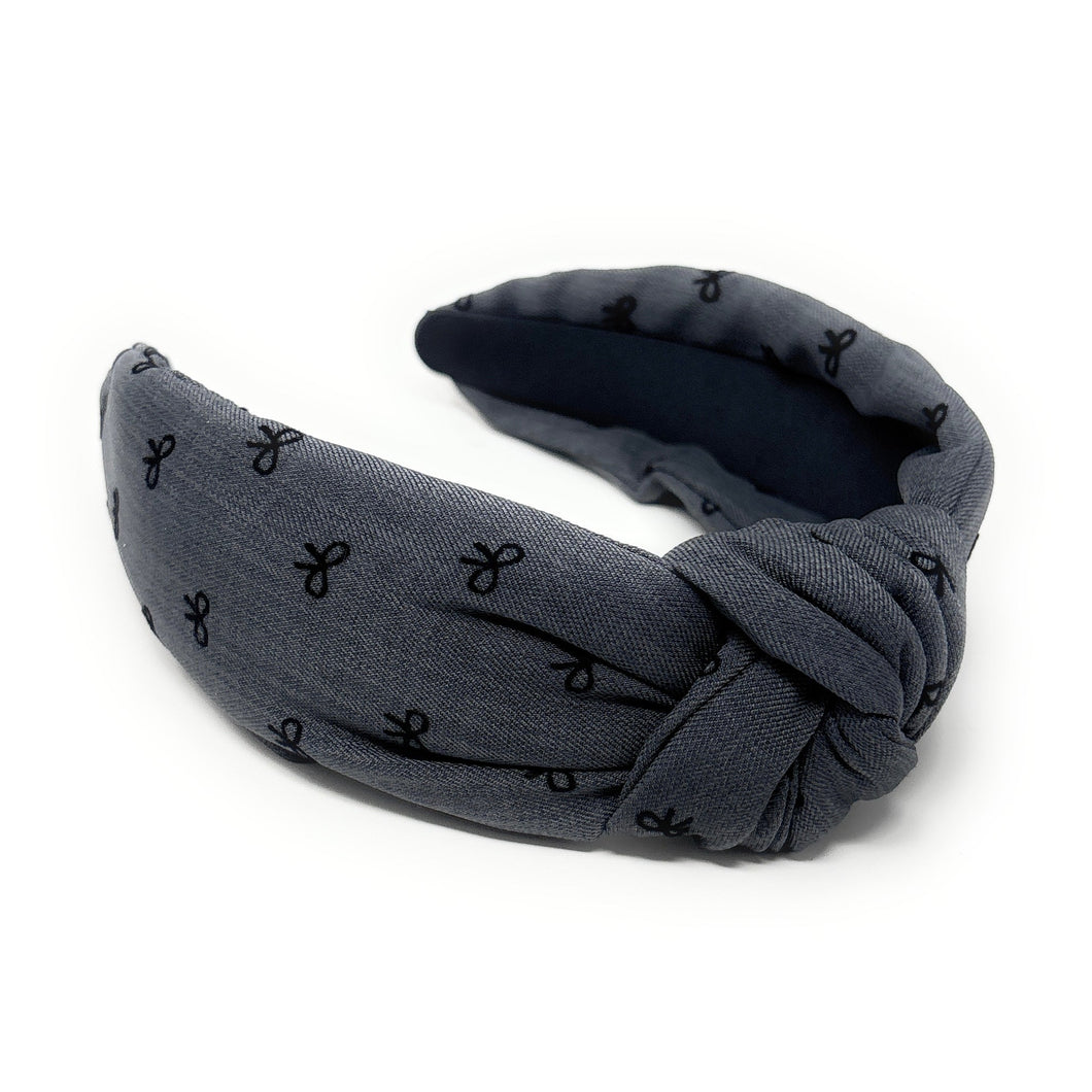 A blue headband with a knotted design, featuring small black bow patterns. The inside tag reads 