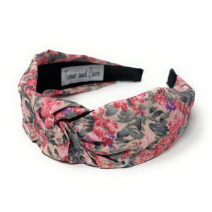 Floral headband with pink, purple, and dark green pattern on a white background. It features a central knot, creating a vibrant, stylish look.