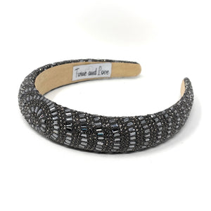 A dark beaded headband with intricate patterns on a white surface. The headband has a textured design and an elegant, luxurious appearance.