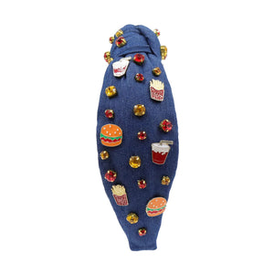 A blue denim headband with a knot design, decorated with red, gold, and clear rhinestones and small enamel fast-food-themed pins, including fries and sodas.